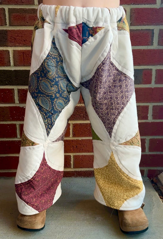 Patchwork pants with colorful patterns worn by a person against a brick wall.