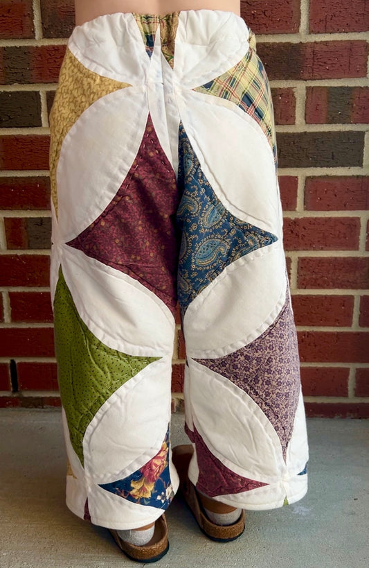 Patchwork pants worn by a person against a brick wall.